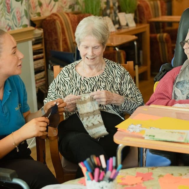 Caregiver assists two elderly women knitting